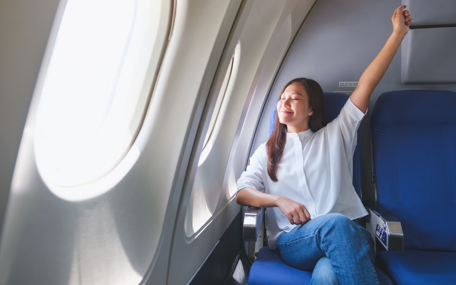 Portrait image of a woman with arm raised traveling on an airplane